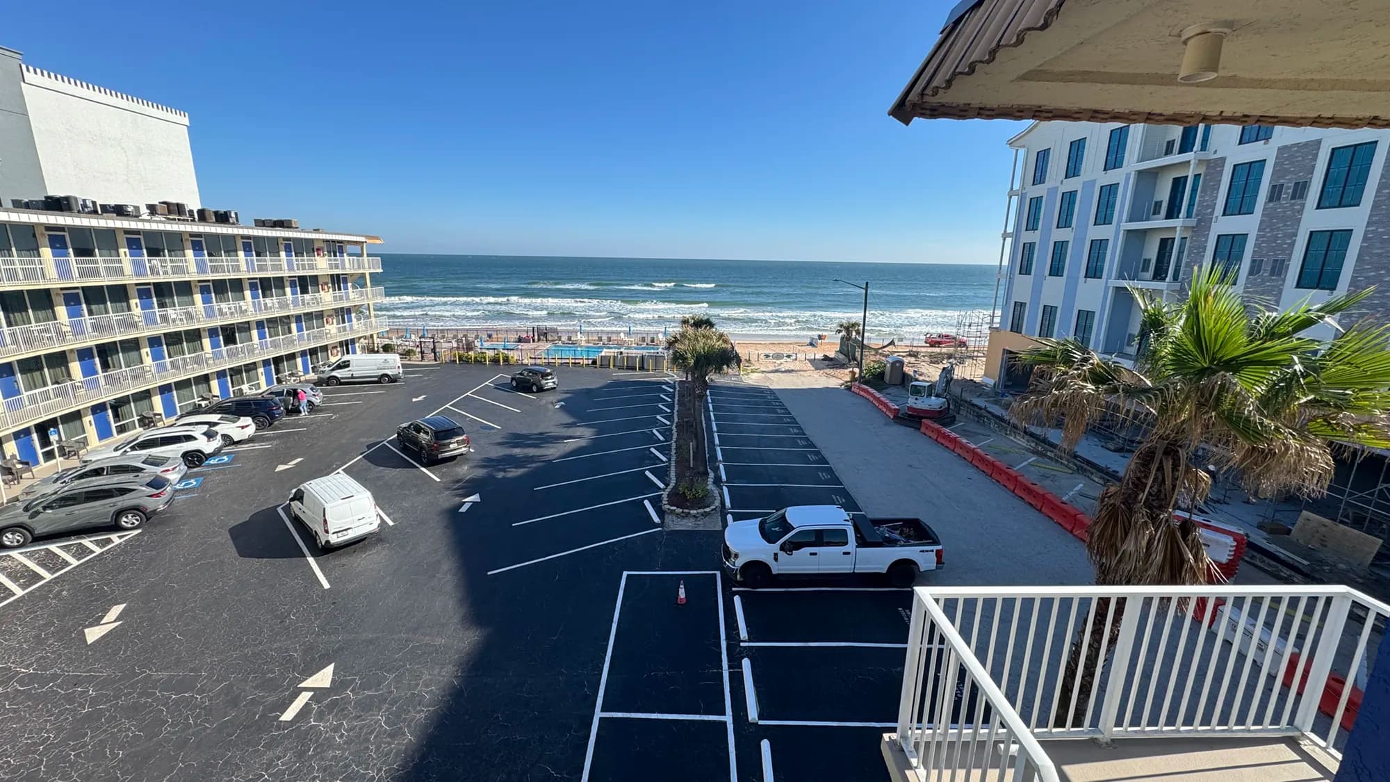 Oceanfront view between two beachfront buildings with parking lot and waves beyond.