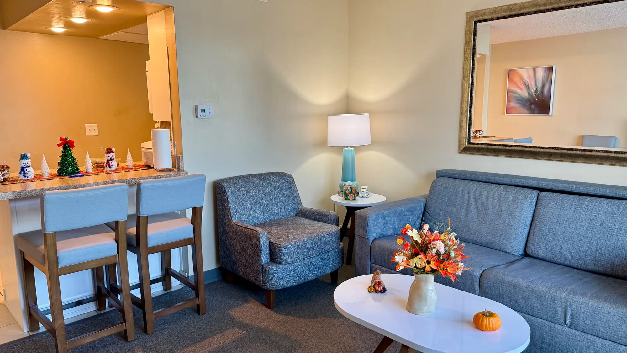 Cozy living room with sofa, armchair, coffee table, and bar seating next to a kitchenette.