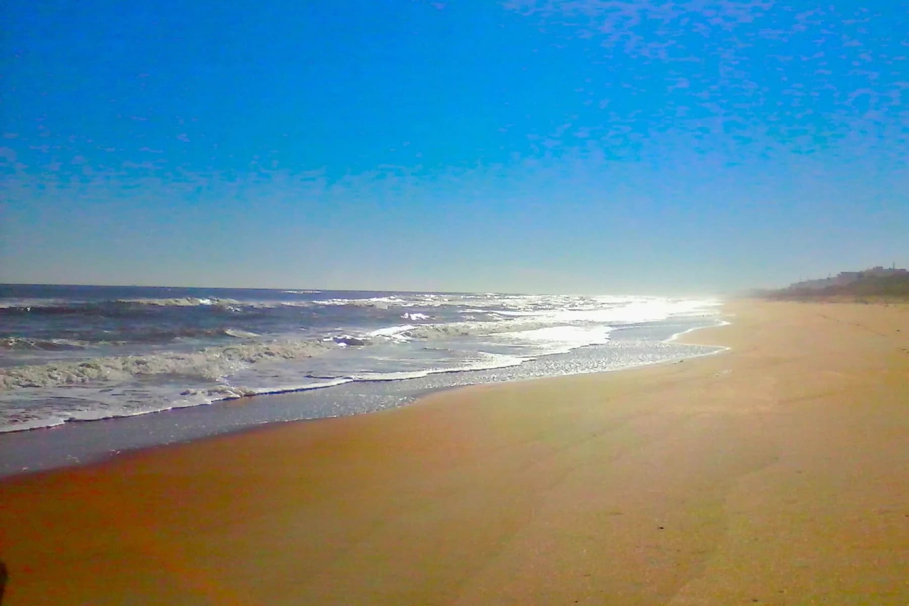 Sandy beach shoreline with gentle ocean waves under a clear blue sky.