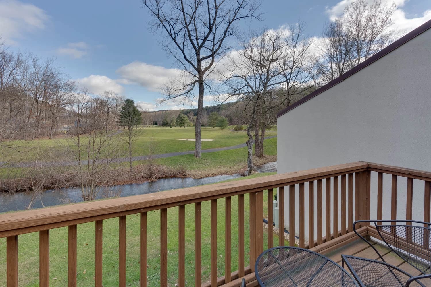 Balcony view overlooking a serene golf course and creek with trees and blue sky.