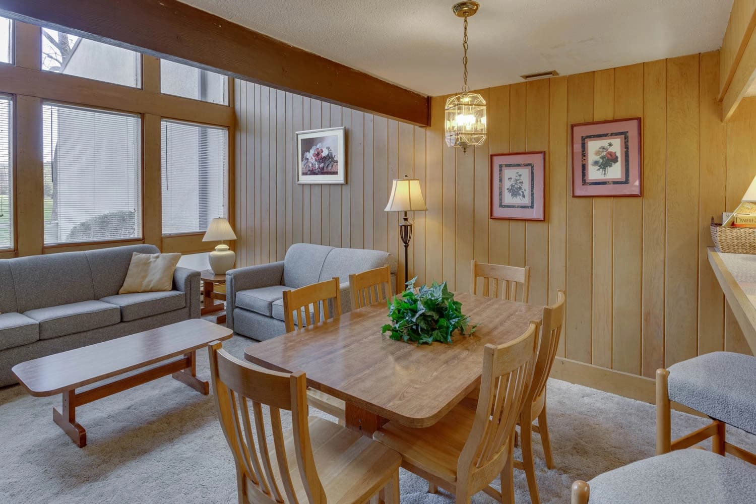 Cozy living and dining area with wooden walls, sofa, armchair, and a wooden dining table.