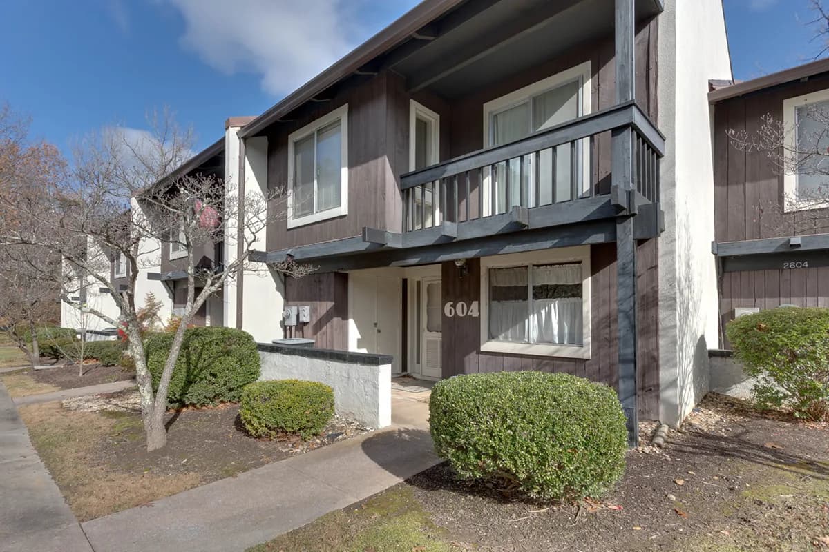 Townhouse with balcony, surrounded by shrubs and bare trees.