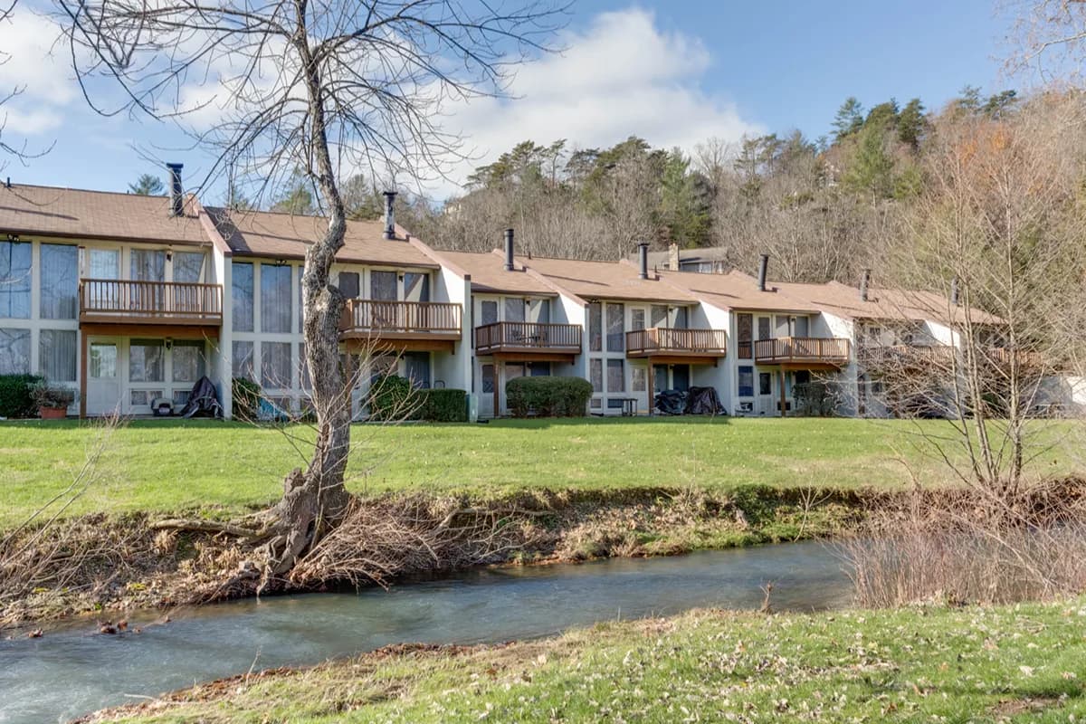 Townhouses with balconies overlooking a stream and lush landscape.